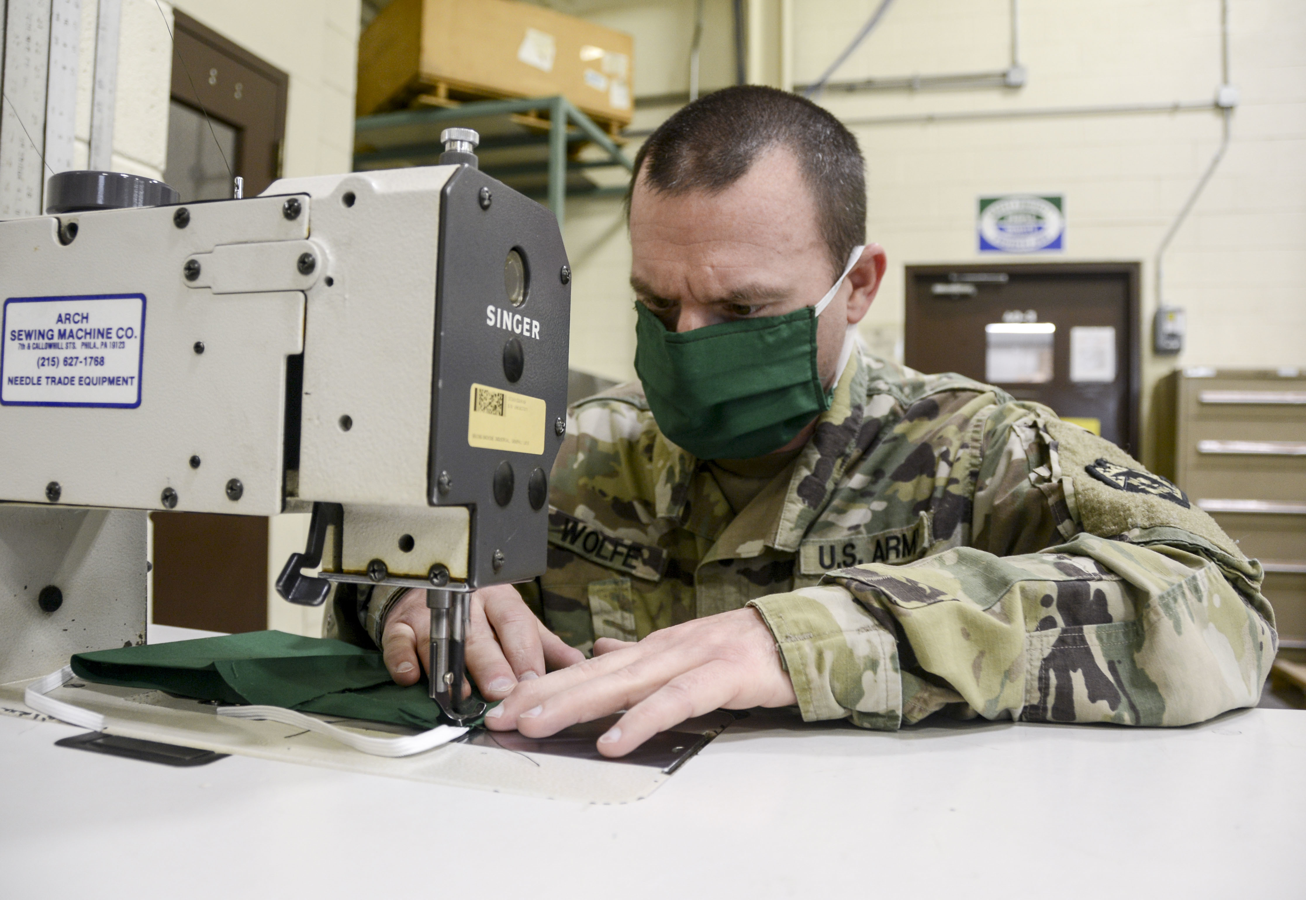 a member of the us army wearing a mask works at a sewing machine