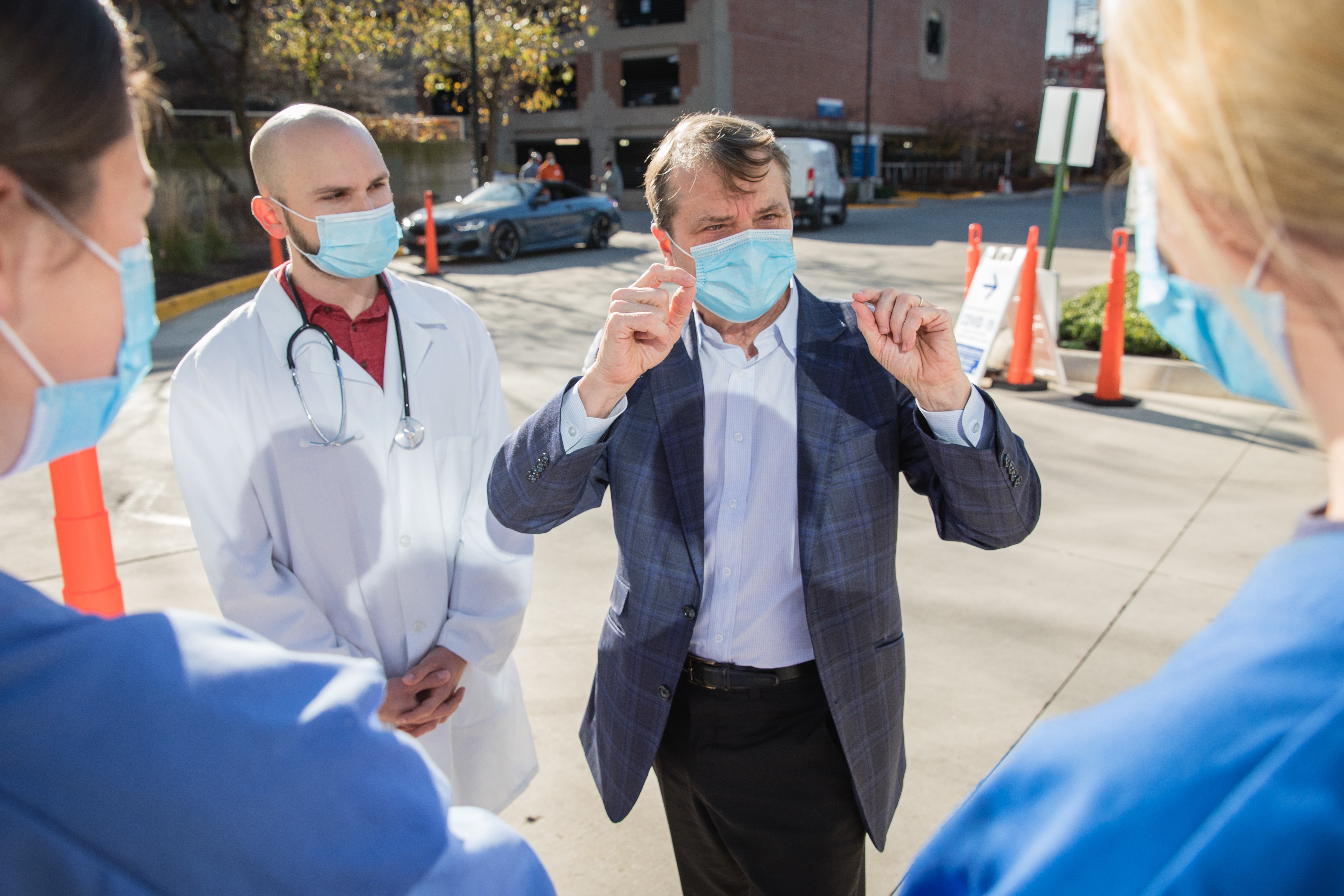 U.S. Rep Mike Quigley, masked, speaks with two women in masks and nursing scrubs, and a man in a doctor's coat, outside a hospital building