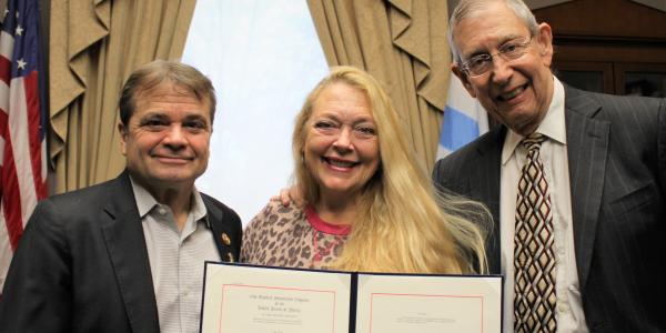 Mike Quigley, Carole Baskin, and Howard Baskin stand together with Carole in the center holding a copy of the Big Cat Public Safety Act