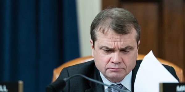 rep quigley looks through papers while sitting at a dais with a placard in front of him