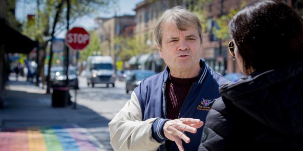 an older white man in a varsity style jacket speaks with a woman with dark hair in front of the famous painted sidewalks in North Halstead in Chicago