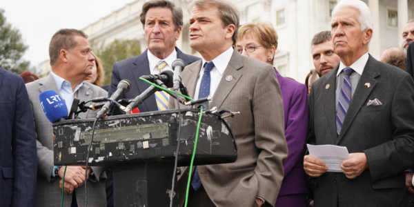 MQ speaks at a podium surrounded by other members of Congress 