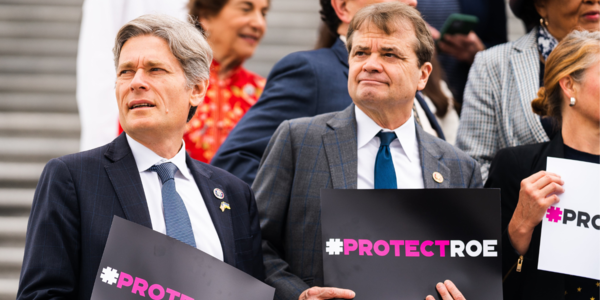 Rep Quigley stands on the steps of the US Capitol holding a ProtectRoe sign surrounded by other members holding signs