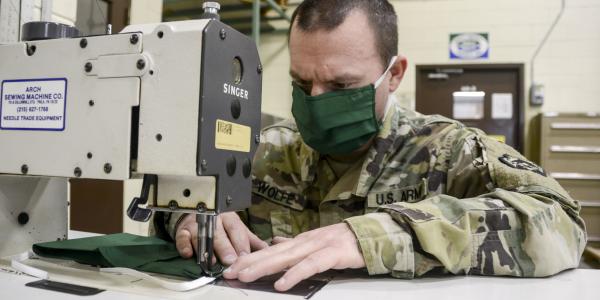 a member of the us army wearing a mask works at a sewing machine
