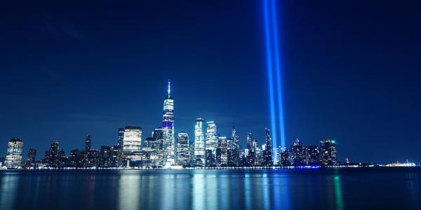 the new york city skyline at night with two light beams pointed toward the sky