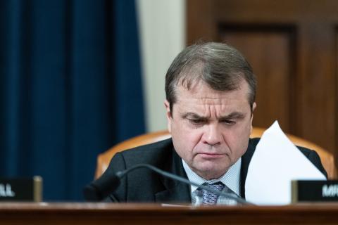 rep quigley looks through papers while sitting at a dais with a placard in front of him