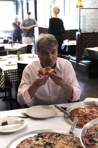 Quigley eating a slice of pizza from Pat's Pizza in Chicago.