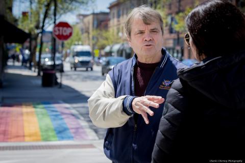 an older white man in a varsity style jacket speaks with a woman with dark hair in front of the famous painted sidewalks in North Halstead in Chicago