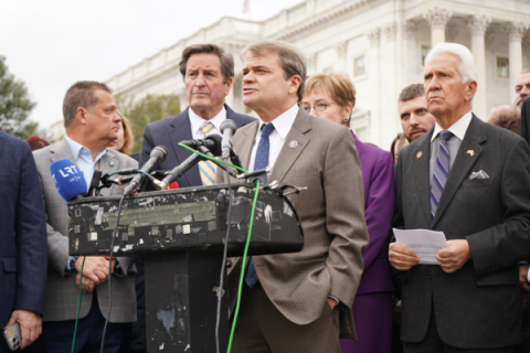 MQ speaks at a podium surrounded by other members of Congress 