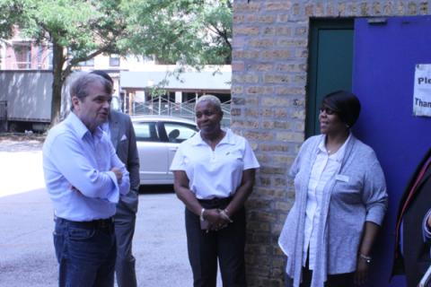 Rep. MikeQuigley stands outside of a brick building in his shirtsleeves, talking with two women in Belray Apartments shirts.