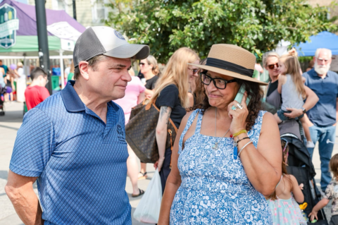 rep quigley talks to a woman in a sundress at a crwoded outdoor event with booth tents in the background