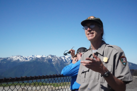 a national park ranger stands in front of a mountain range in olympic national park
