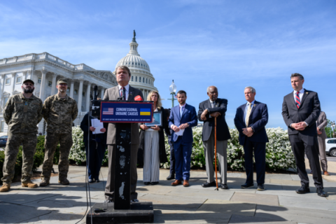 Rep. Quigley stands at a podium in front of the US Capitol flanked by men in military uniform and members of Congress