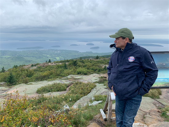 Congressman Mike Quigley stands on a rocky slope and looks into the distance. In the background, the ocean and small islands are visible.