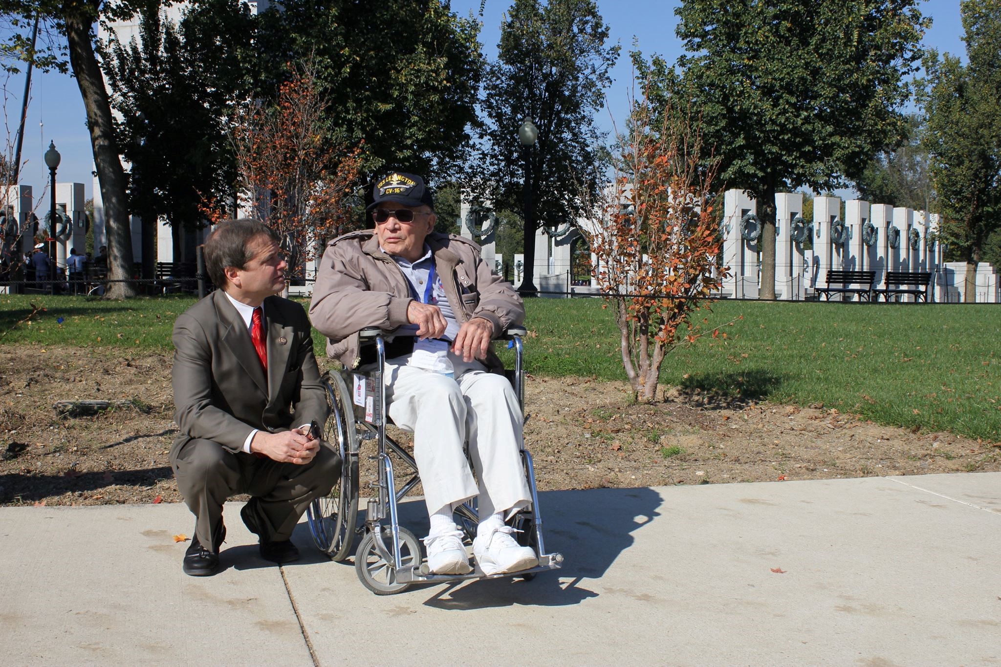Rep. Quigley kneels on the ground to speak with a veteran in a wheelchair near the World War II Memorial in Washington, DC during an Honor Flight visit