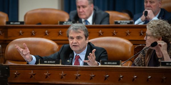 Quigley at a wooden dias gesticulating angrily