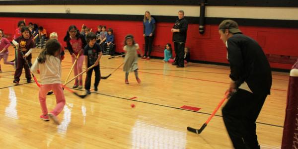 Rep Quigley plays hockey with a group of children in a YMCA gym