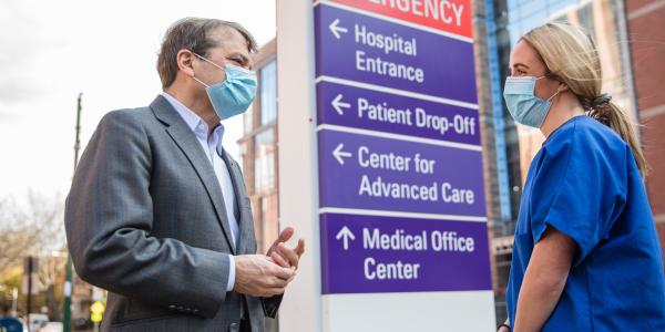 Congressman Mike Quigley wears a suit and facemask speaking with a woman in blue scrubs in front of a COVID testing sign