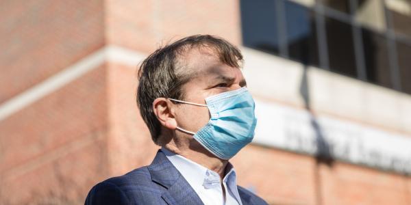 Rep. Mike Quigley is seen in profile wearing a suit and surgical face mask, he stands in front of a red brick building