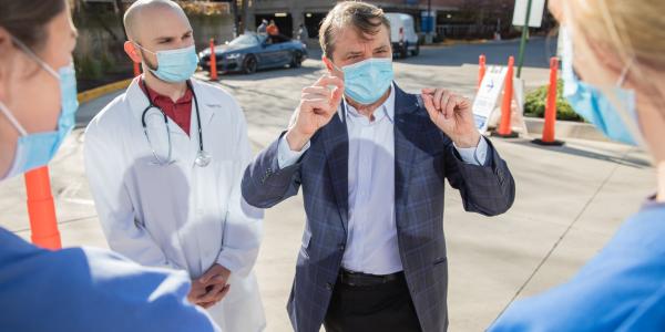 U.S. Rep Mike Quigley, masked, speaks with two women in masks and nursing scrubs, and a man in a doctor's coat, outside a hospital building