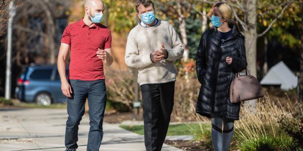 Mike Quigley walks down a sidewalk with a man and woman, all wearing masks, they are gesturing as though in conversation