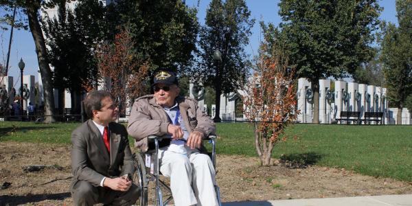 Rep. Quigley kneels on the ground to speak with a veteran in a wheelchair near the World War II Memorial in Washington, DC during an Honor Flight visit